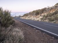 an empty winding road on a mountain with the sun set above the mountains in the background