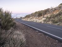 an empty winding road on a mountain with the sun set above the mountains in the background