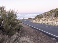 an empty winding road on a mountain with the sun set above the mountains in the background