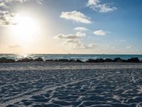 three people standing on beach looking out at sea with waves rolling towards them and sun