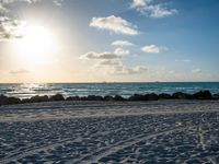 three people standing on beach looking out at sea with waves rolling towards them and sun