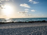 three people standing on beach looking out at sea with waves rolling towards them and sun