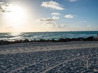 three people standing on beach looking out at sea with waves rolling towards them and sun