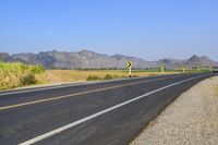 three yellow and white signs near a highway with mountains in the background in front of them