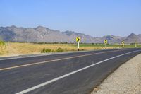 three yellow and white signs near a highway with mountains in the background in front of them