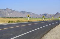 three yellow and white signs near a highway with mountains in the background in front of them