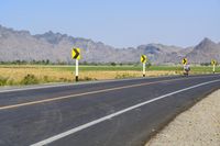 three yellow and white signs near a highway with mountains in the background in front of them