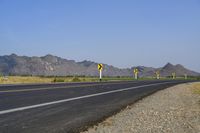 three yellow and white signs near a highway with mountains in the background in front of them