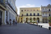 three young people are walking down a city square in front of old buildings and palm trees
