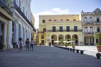 three young people are walking down a city square in front of old buildings and palm trees