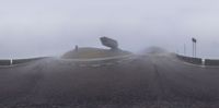 someone standing on a hill while holding up umbrellas in the rain, under a foggy sky