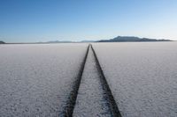 the tire tracks of cars on snow covered ground in the desert with mountains in the distance