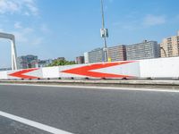 a car driving over a bridge on the side of the road near some buildings with red arrows