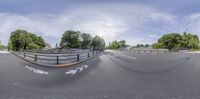 a fisheye lens view of an intersection with a bike lane, buildings and green trees