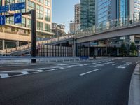 an empty road with a street sign at the curb in front of an office building