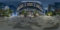 a very large circular building near many buildings at night time and some people walking in it