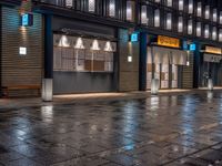 a large brick sidewalk with a store front at night time and a sign that says