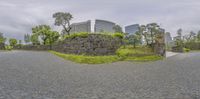 a large stone wall in the middle of a paved road surrounded by green trees and tall buildings