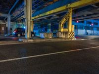 the car is parked underneath an overpass at night time, while no other cars are present