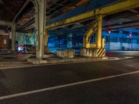 the car is parked underneath an overpass at night time, while no other cars are present