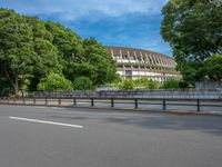 a view of a stadium from the street, showing many trees and bushes in the distance