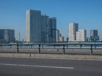 the highway and bridge leading to a city in japan and has tall buildings and blue skies