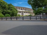 a view of a stadium from the street, showing many trees and bushes in the distance