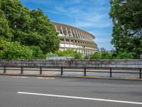 a view of a stadium from the street, showing many trees and bushes in the distance