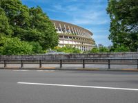 a view of a stadium from the street, showing many trees and bushes in the distance