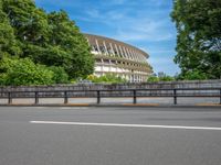 a view of a stadium from the street, showing many trees and bushes in the distance