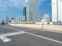 the view from a bus windshield on an empty freeway with tall buildings on both sides and a blue sky in the background