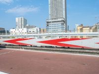 a red and white train traveling down a track near tall buildings overpassed in the background