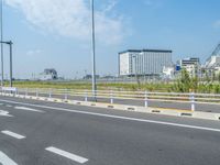 a picture of an empty highway with white lines on it and buildings in the background