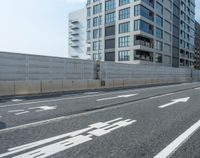 an empty street with a wall and bicycle lane sign on it's side next to some large buildings