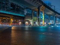 street lights on an empty city street at night under an overpassed highway, with cars