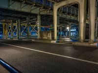 the car is parked underneath an overpass at night time, while no other cars are present