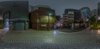 some buildings and people walking around on a street at night, and a full fish eye lens