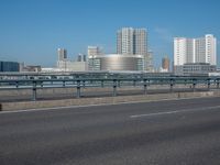 the highway and bridge leading to a city in japan and has tall buildings and blue skies