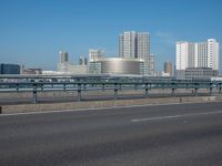 the highway and bridge leading to a city in japan and has tall buildings and blue skies