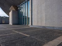 a sidewalk that has several glass doors next to it with buildings in the background behind