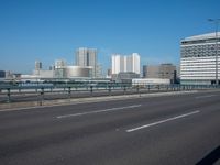 the highway and bridge leading to a city in japan and has tall buildings and blue skies