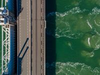 a bridge over the ocean with construction equipment in the background and two people walking on it