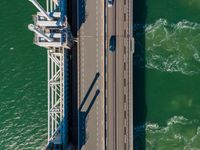 a bridge over the ocean with construction equipment in the background and two people walking on it