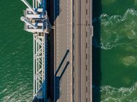 a bridge over the ocean with construction equipment in the background and two people walking on it