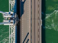 a bridge over the ocean with construction equipment in the background and two people walking on it