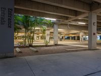 an empty parking garage at night with trees and palm trees in the foreground and a light that reads entrance