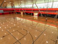 the empty basketball court has many windows above it, some red walls in the background