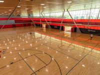 the empty basketball court has many windows above it, some red walls in the background