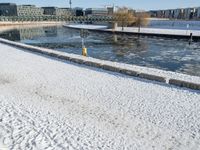 the man is walking along a frozen river bank with an empty bench and a fire hydrant