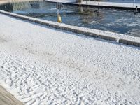 the man is walking along a frozen river bank with an empty bench and a fire hydrant